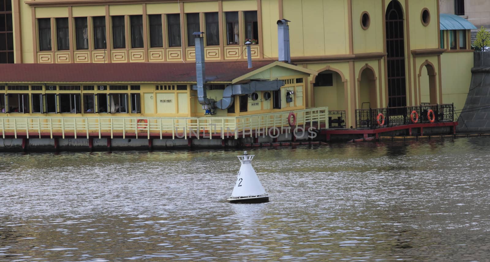 buoy on the river on a gray background waves. In the background, building on the banks of yellow with a brown roof