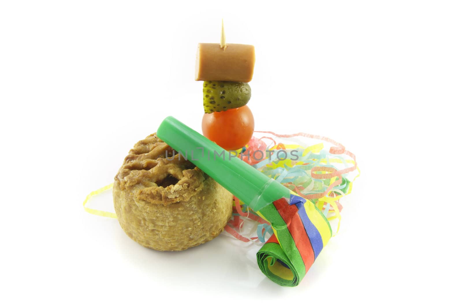 Small pork pie with party blower and cocktail stick containing hot dog sauage, gherkin and tomato with streamers on a reflective white background