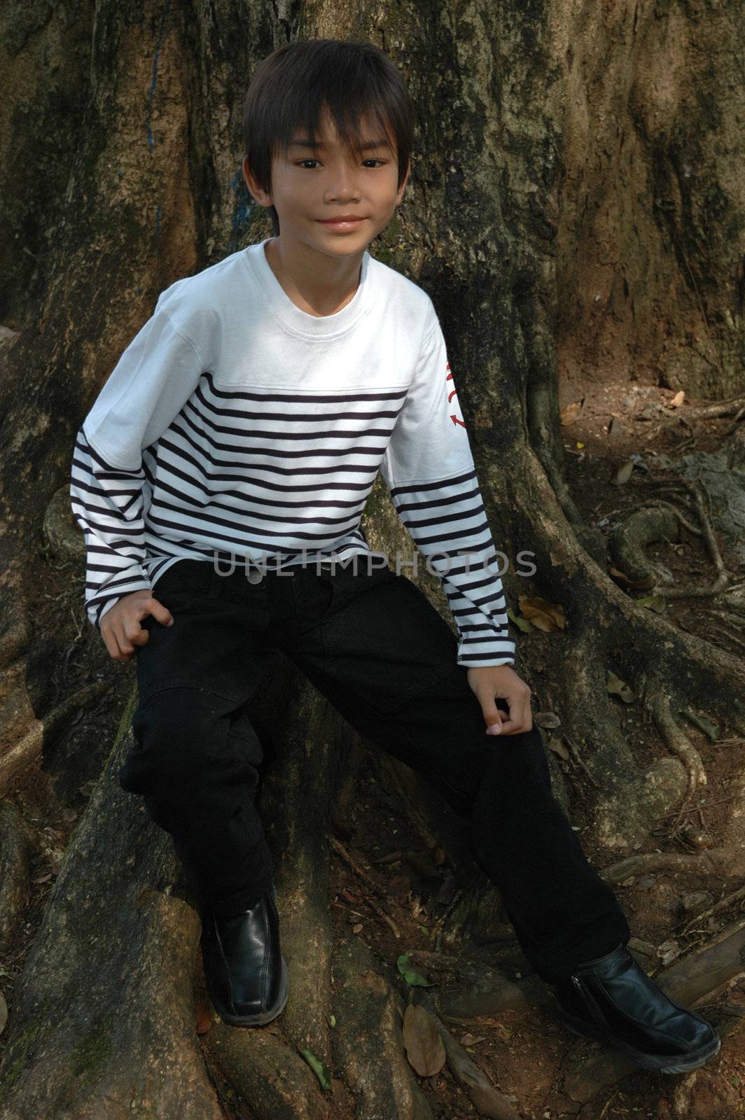 little asian boy sit down beside the tree in park