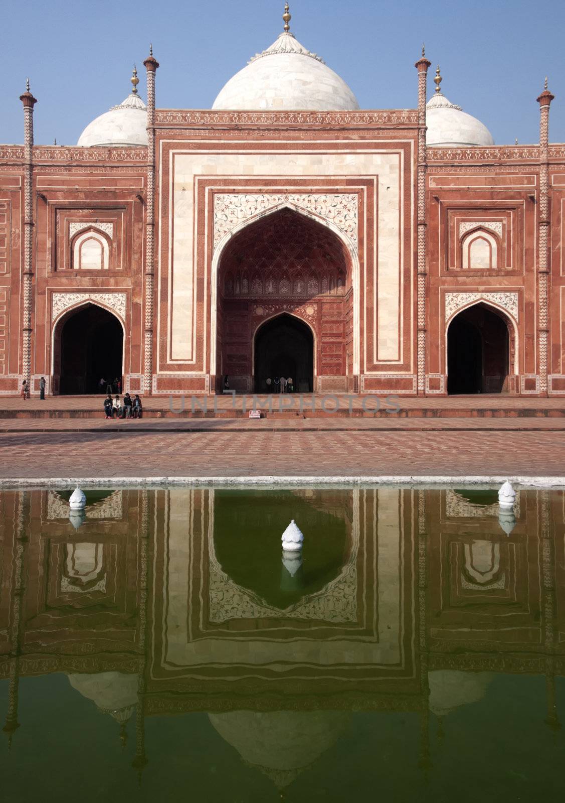 Green water mirrors red sandstone mosque with white domes and decorations.