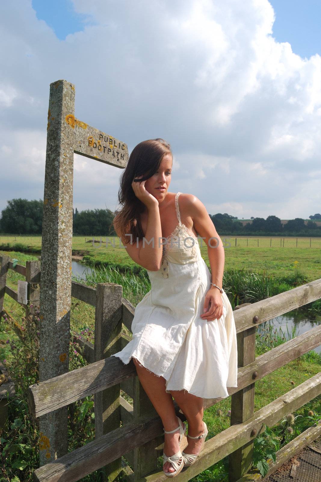 Pretty girl sitting on fence by footpath sign