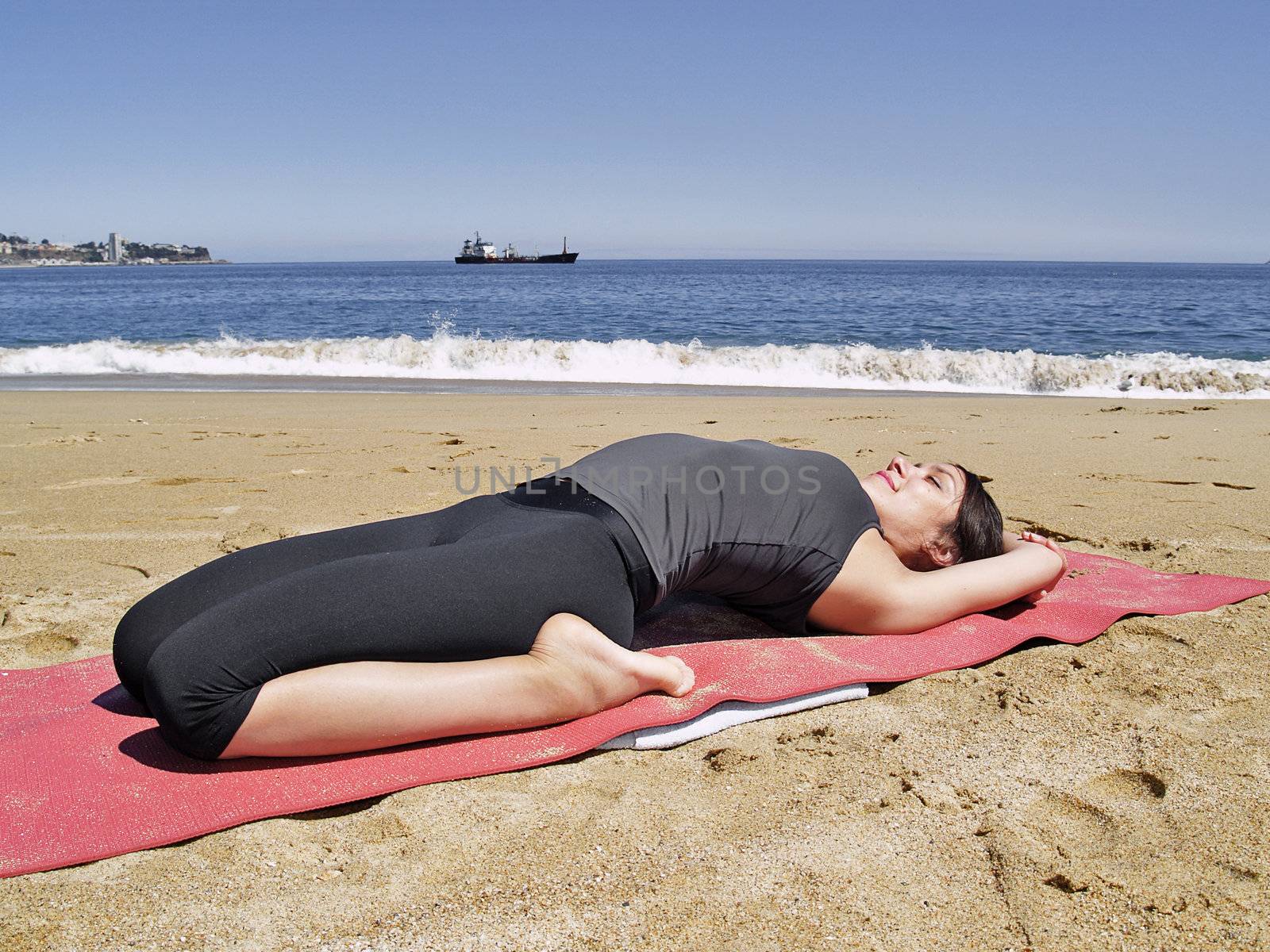 Yoga teacher practising at the beach pose supta bajrasana