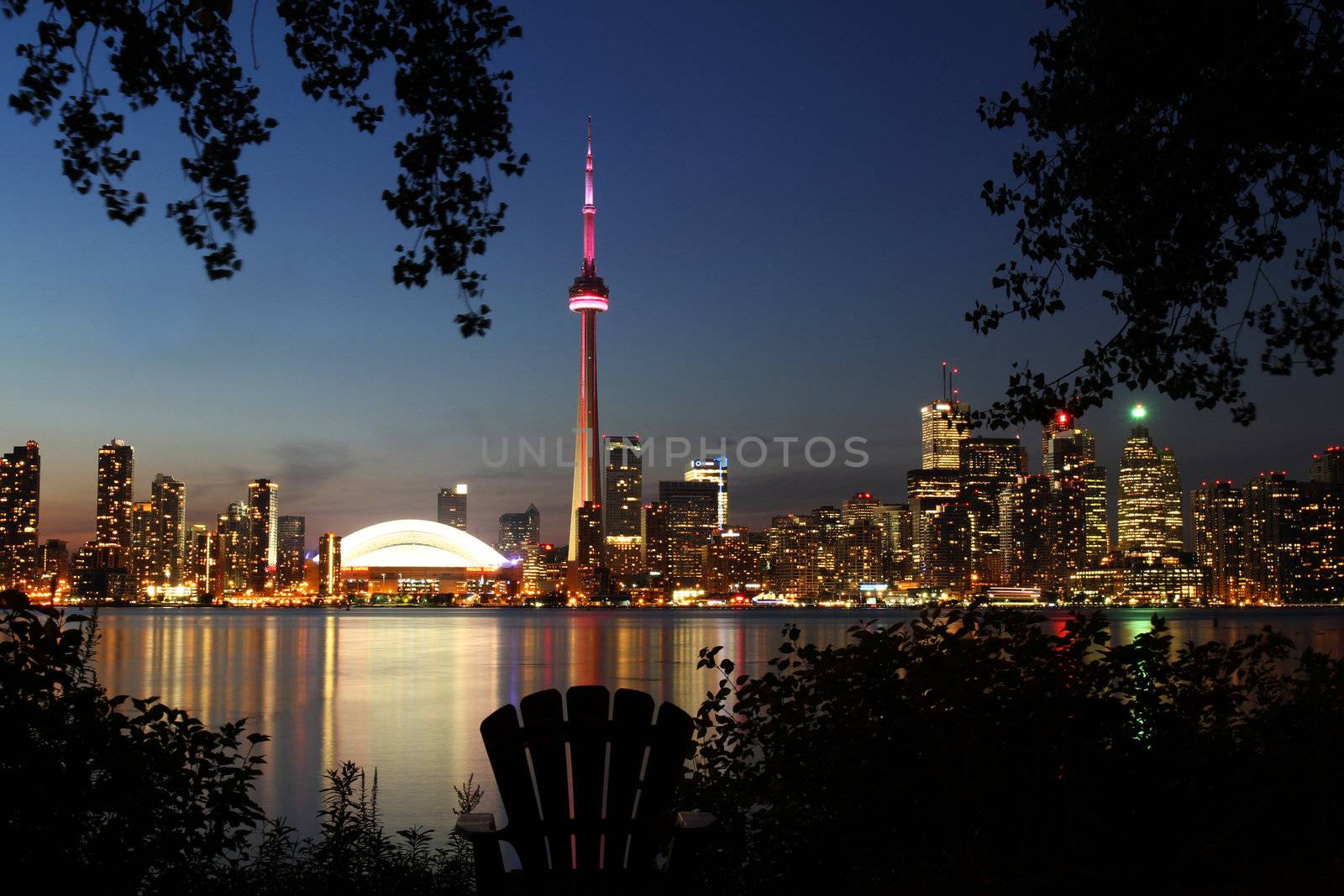 Toronto, Canada - August 12, 2011:  The skyline of Toronto after sunset framed by the silhouette of trees and a Muskoka chair with a view of the city.