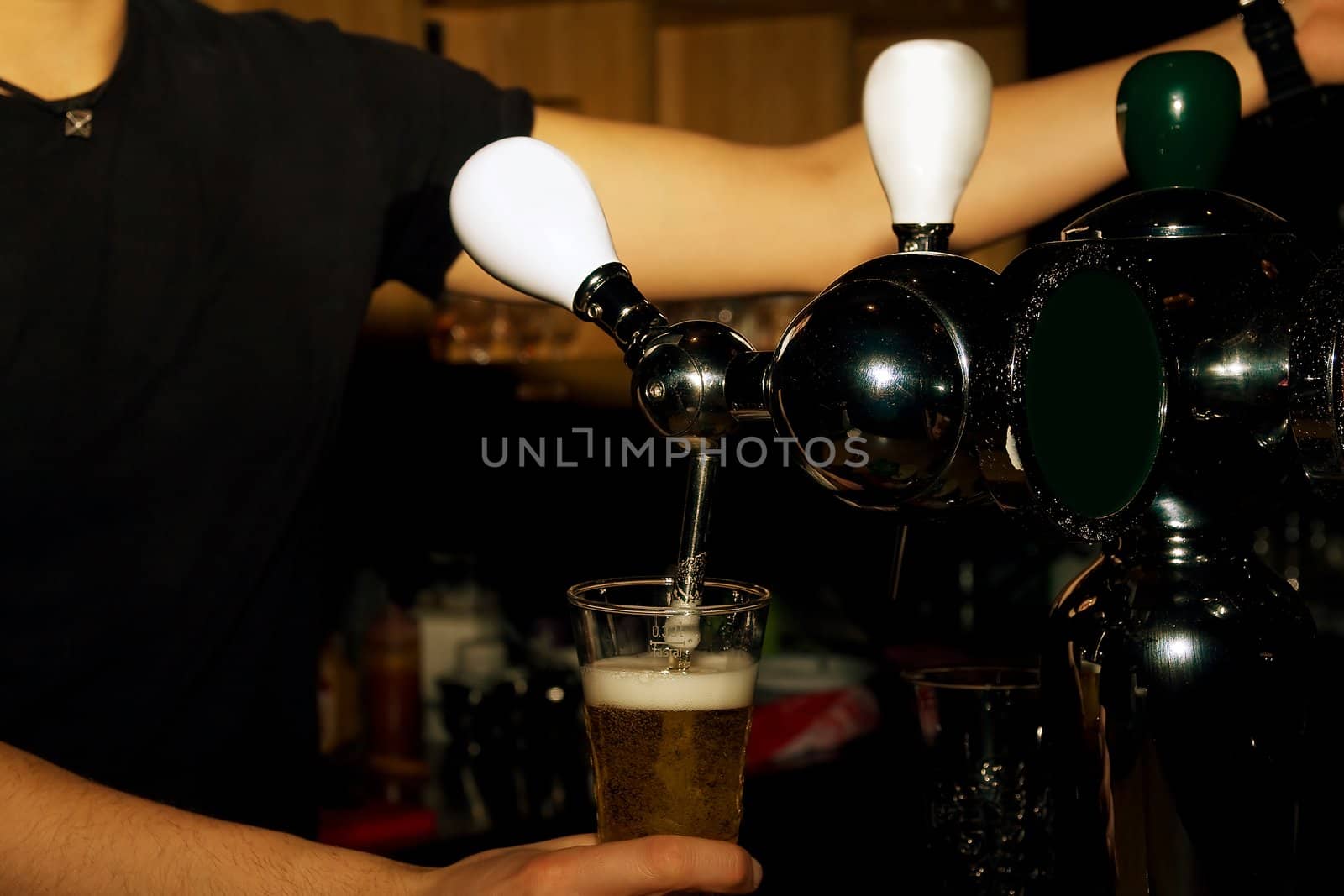 Hands of the bartender pouring beer from cranes in  mugs