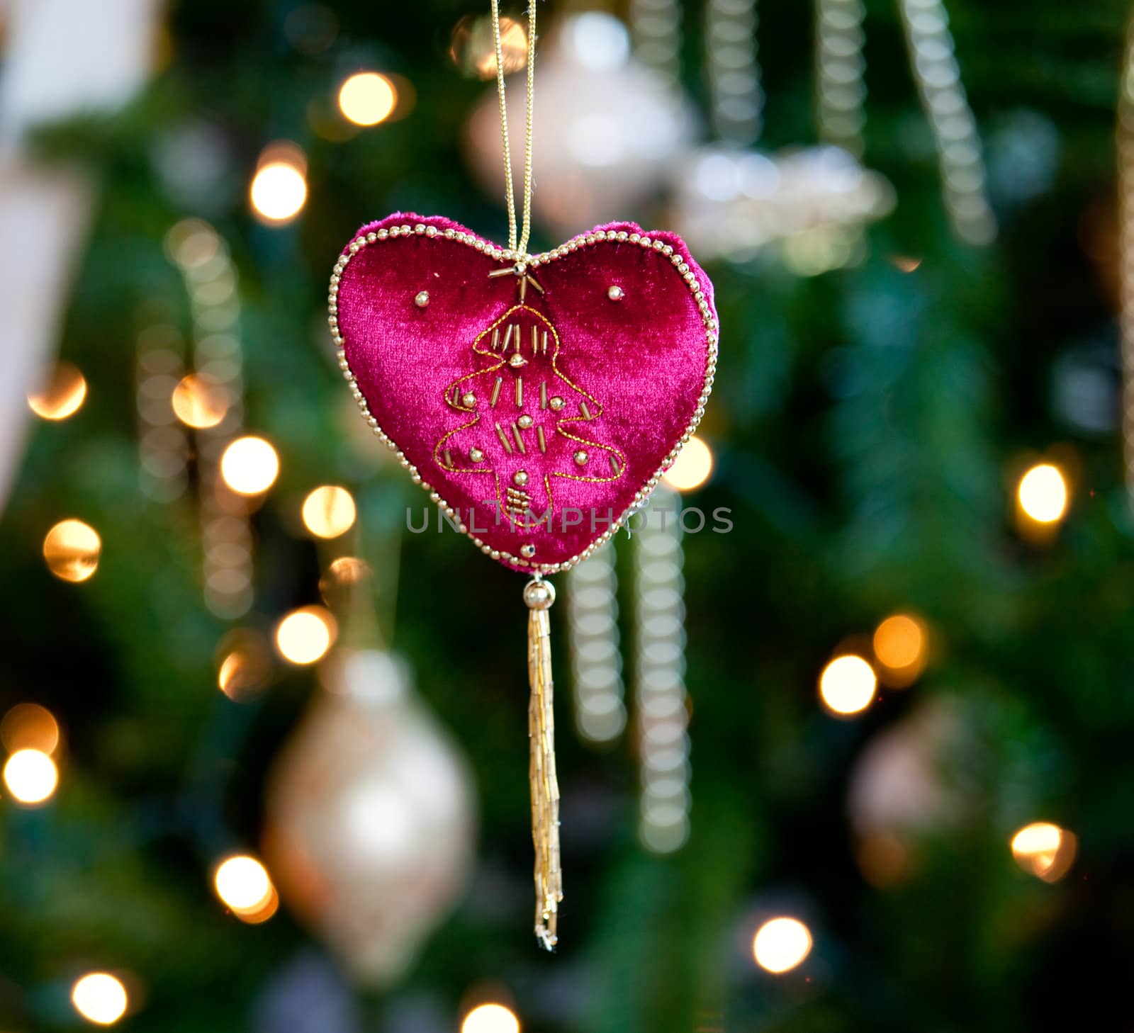 Close up of red velvet heart ornament in front of out of focus christmas decorations