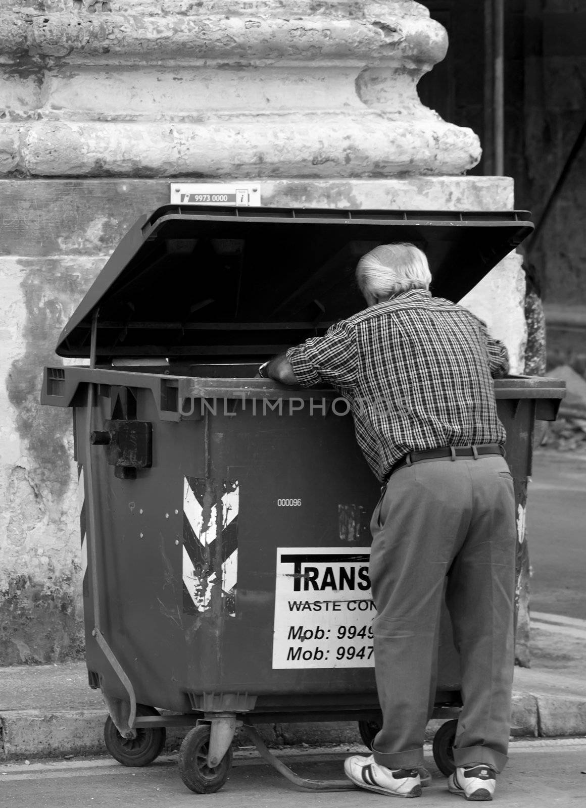 Old man in street in Malta, looking for something in a rubbish tip   