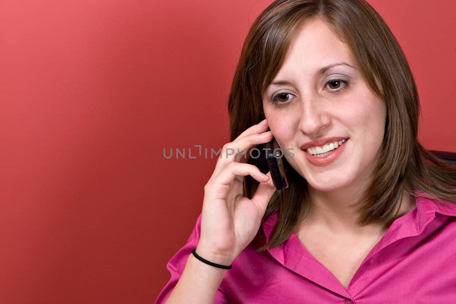 A young business woman talking on her cell phone isolated over a red background.