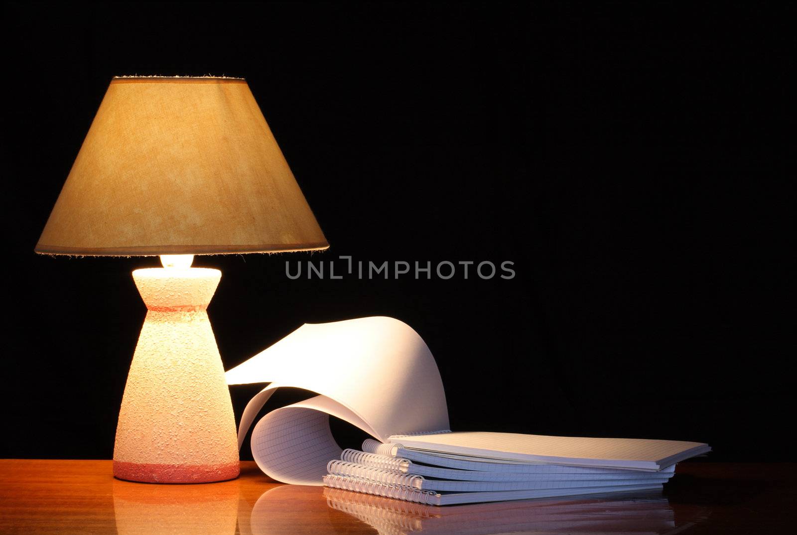 Vintage table lamp with shade near open spiral notebooks on dark background