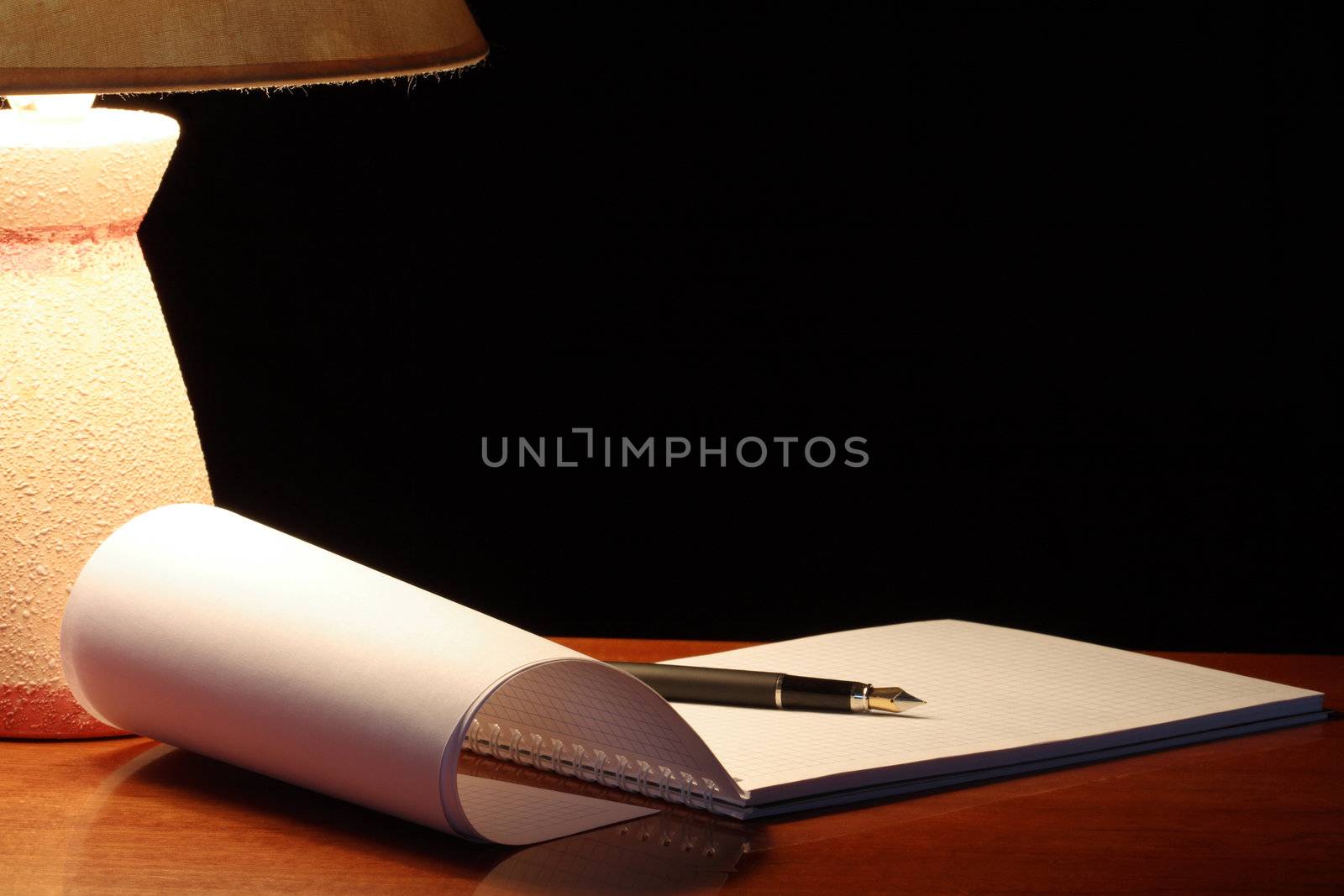 Vintage table lamp with shade near open spiral notebook on dark background