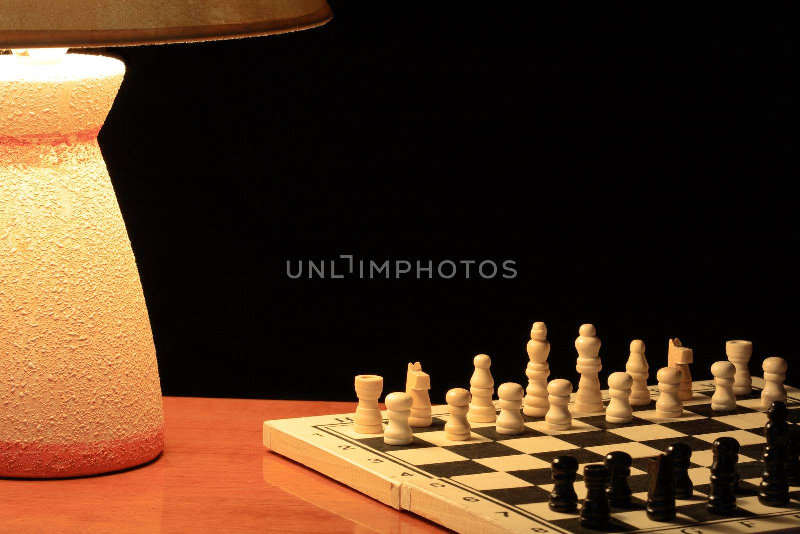 Luminous table lamp standing near chess board on dark background