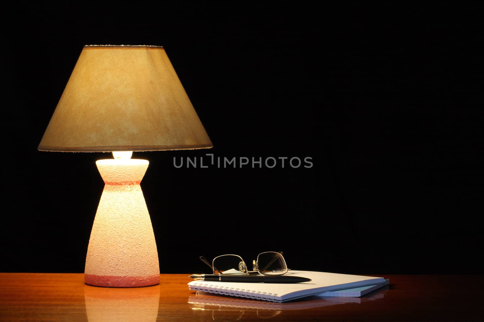 Vintage table lamp with shade near open spiral notebook on dark background