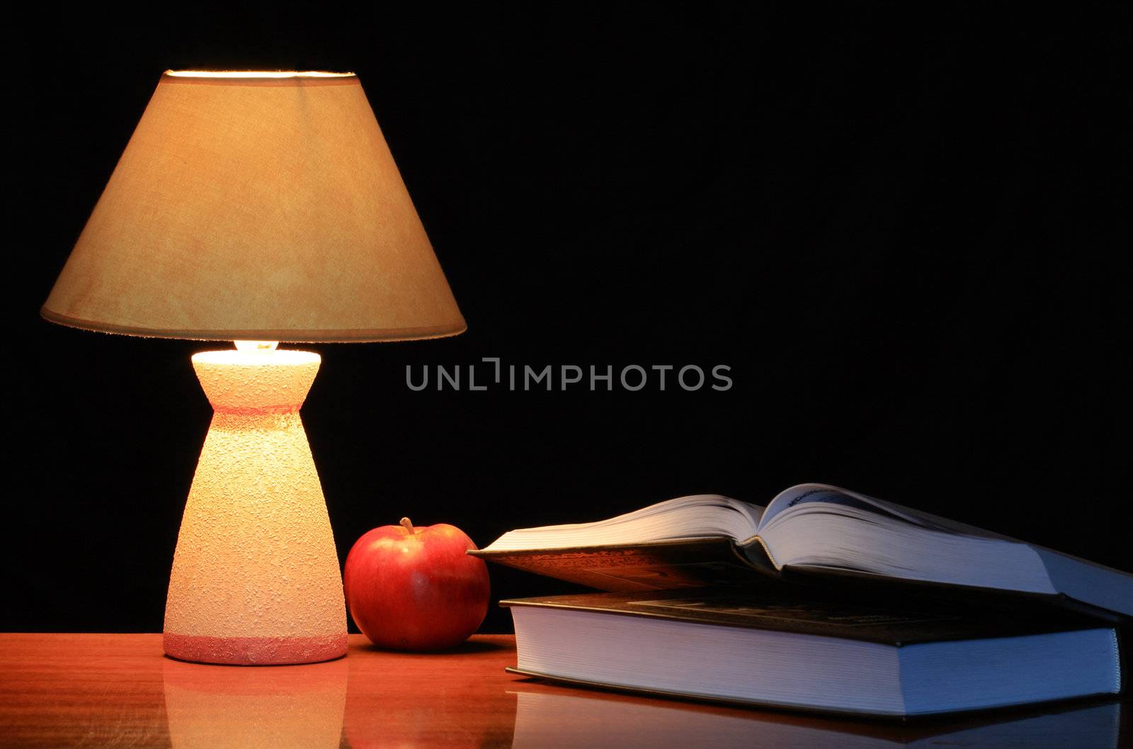 Luminous lamp standing on the table near red apple and two books on dark background with copy space