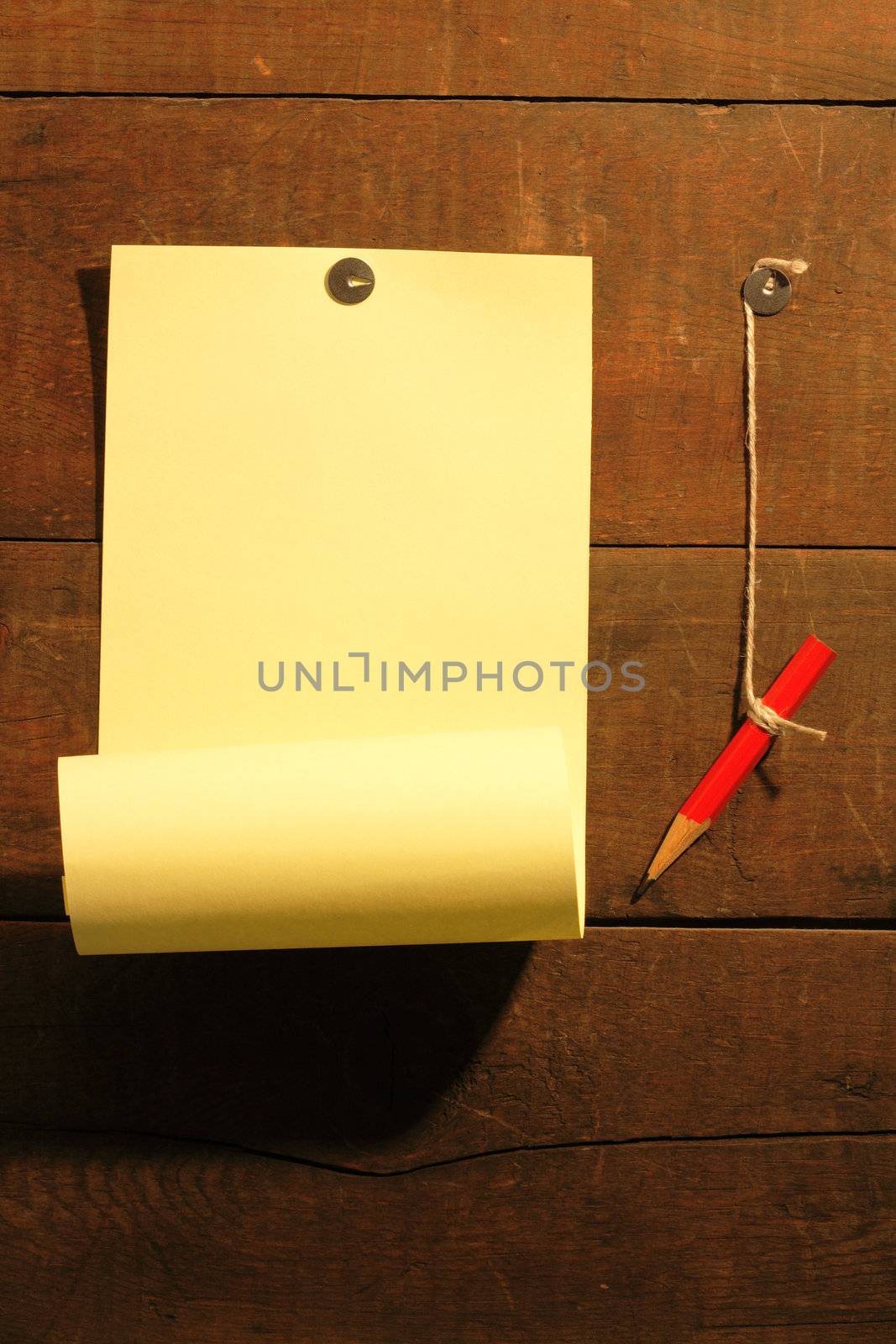 Yellow paper and red pencil hanging on wooden background with thumbtacks