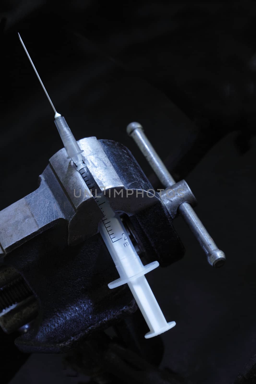 Cracking syringe inside old vise grip on dark background with copy space