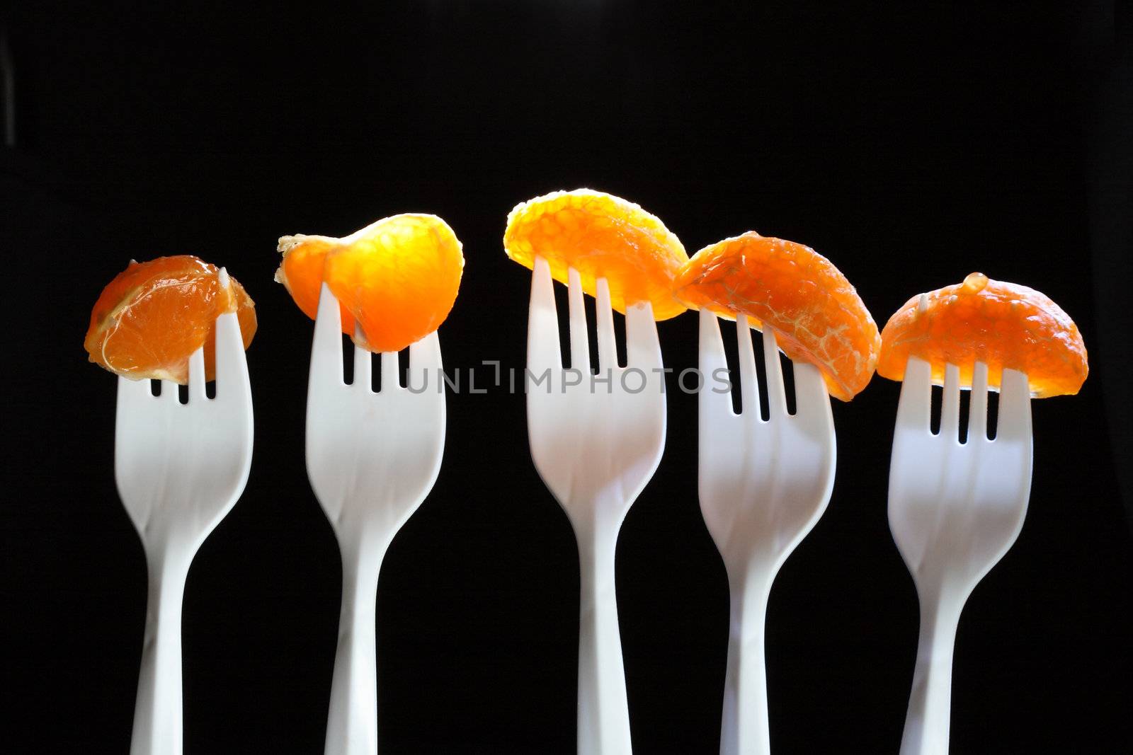 Five white plastic forks with tangerine segments on dark background