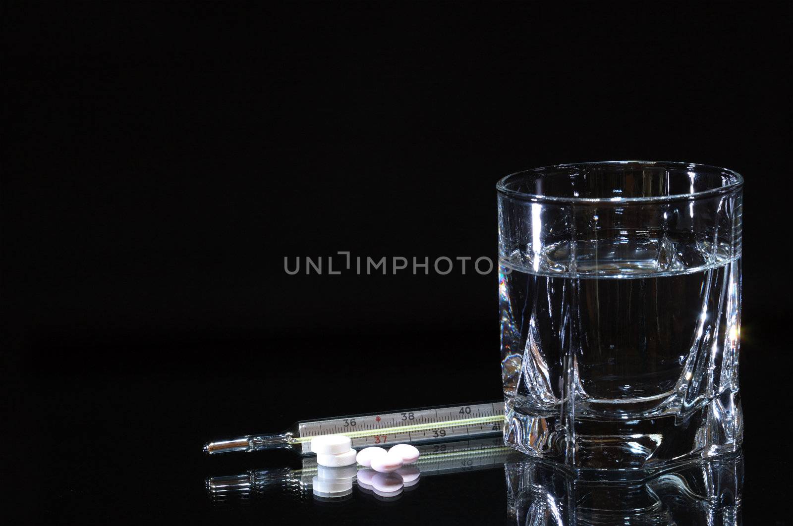 Few pills and thermometer lying near glass of water isolated on dark background with copy space
