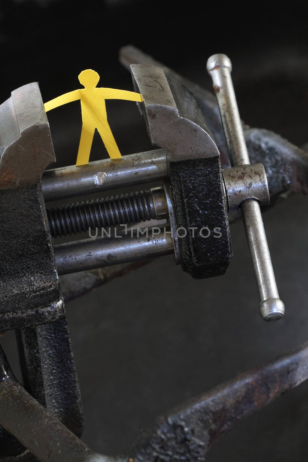 Small yellow paper man under pressure with old vise grip on abstract industry background