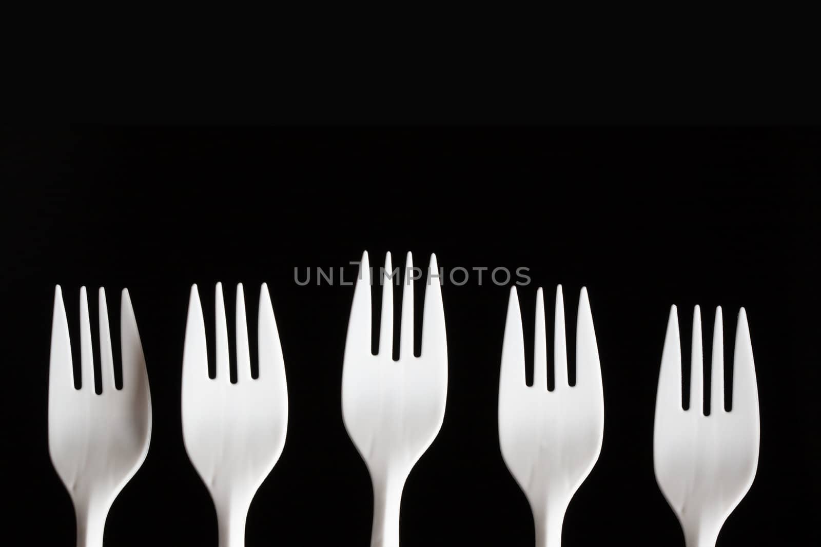 Five white plastic forks in a row shot on a black background