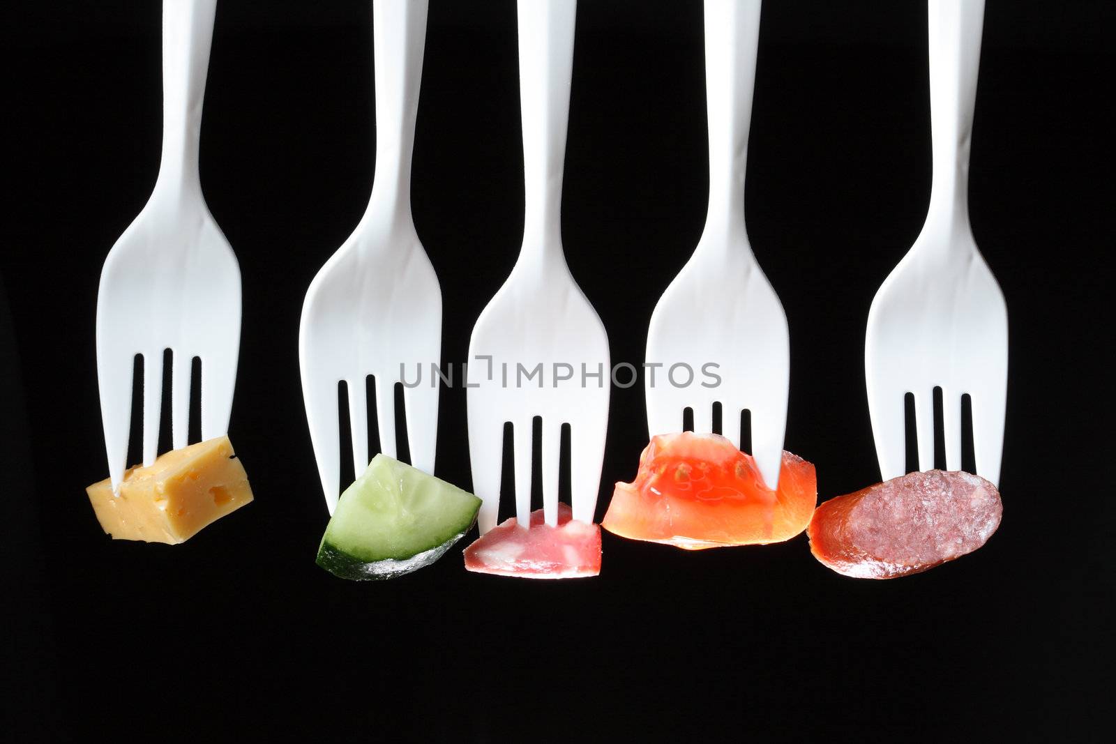 Five white plastic forks in a row with various food on a black background