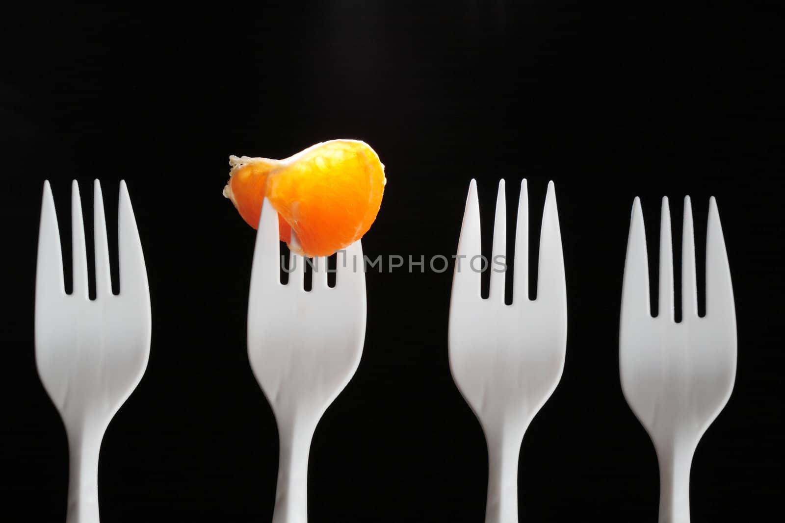 Four white plastic forks on dark. One fork with tangerine segment