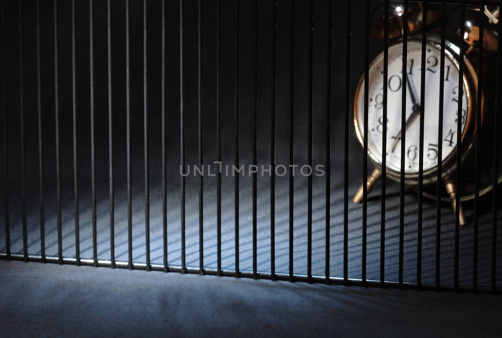 Alarm clock behind bars on dark background with copy space