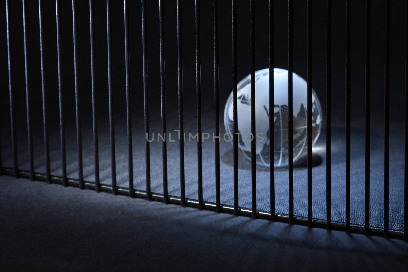 Glass globe behind bars on dark background with copy space
