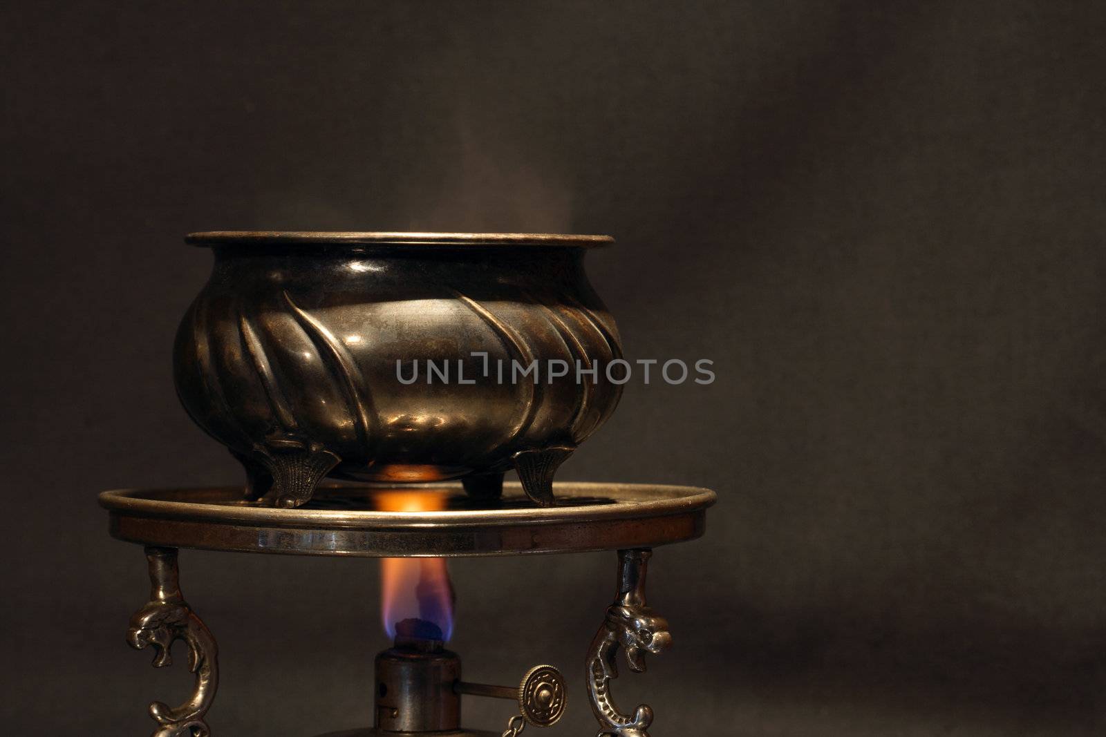 Ancient brass jug standing on vintage table spirit lamp with flame