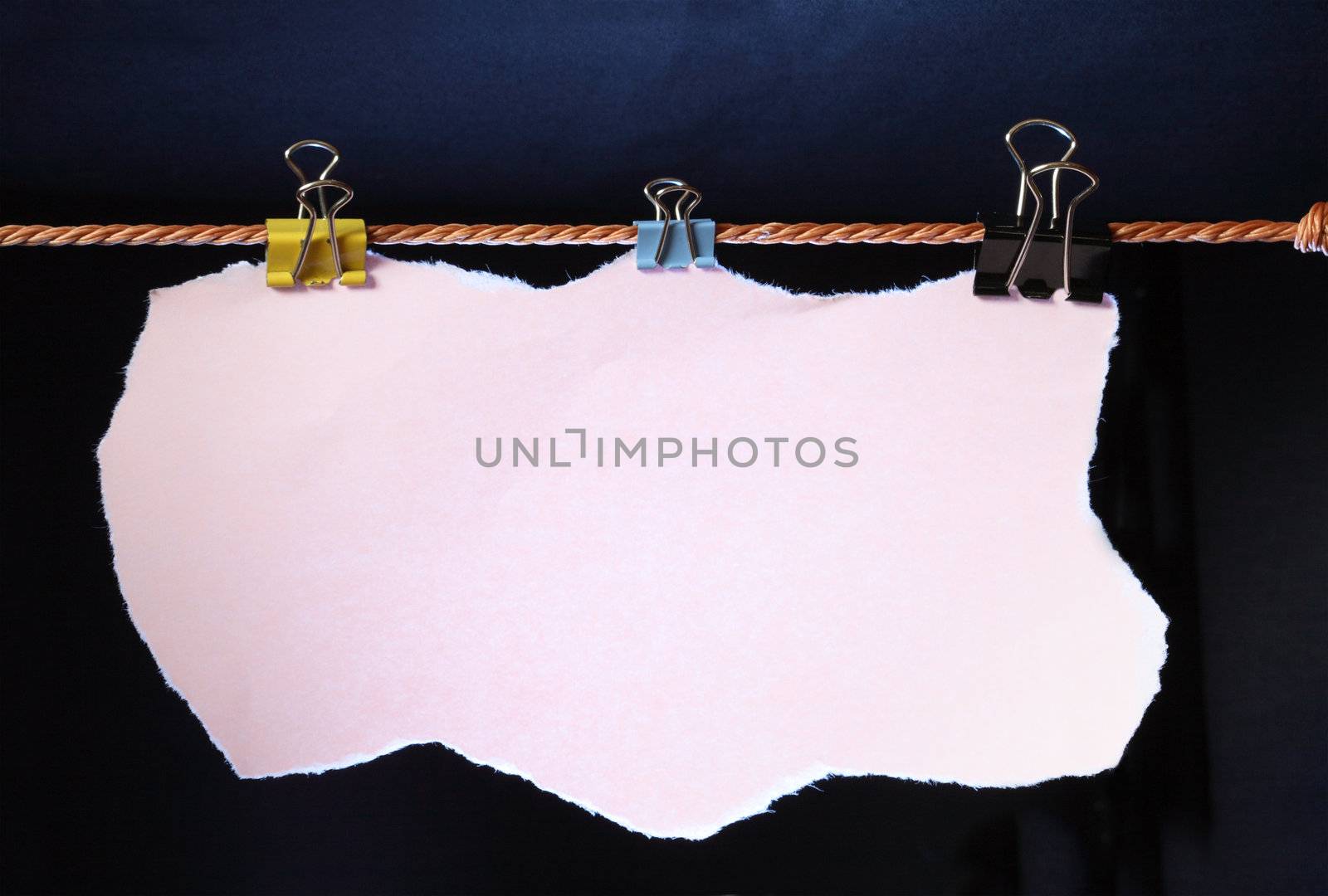 Blank pink paper sheet for your notes hanging on dark background with rope