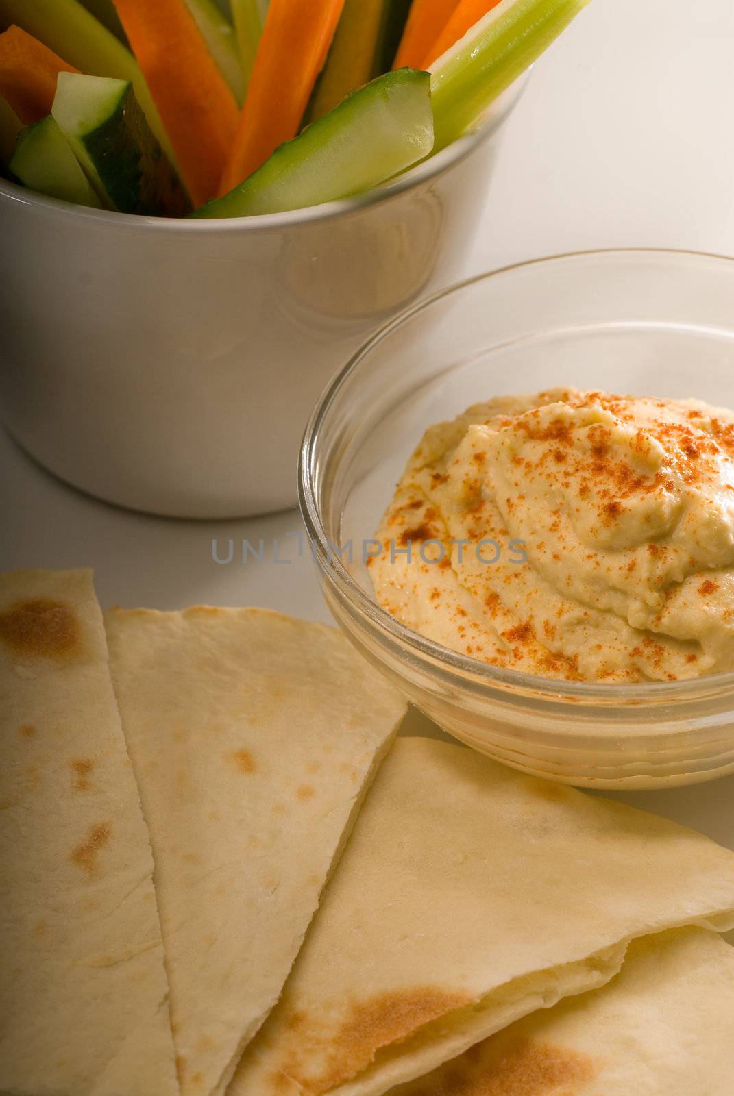 middle eastern hummus dip on a glass bowl with homemade pita bread and raw vegetable