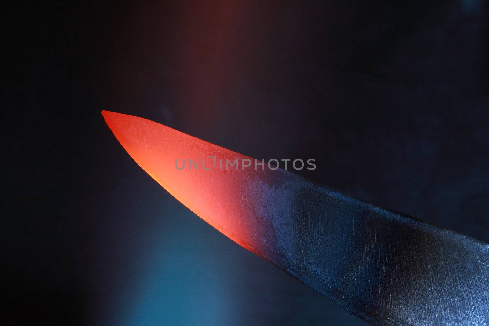 Abstract dark background with closeup of red-hot knife in flame