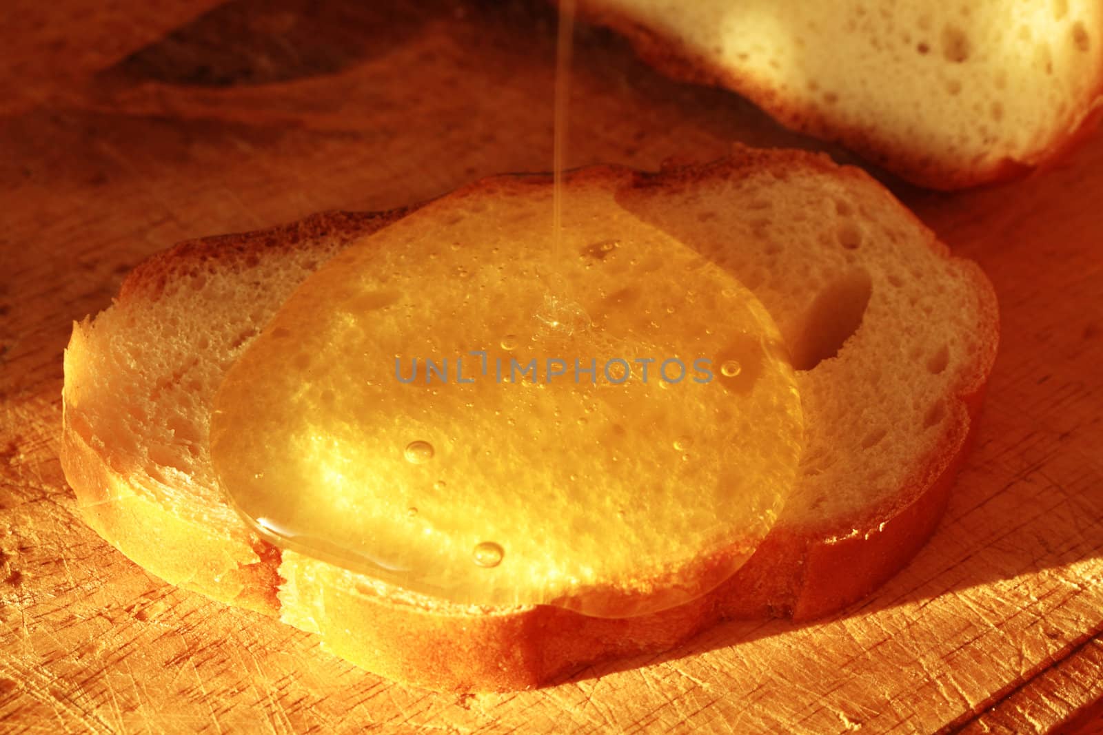 Closeup of honey dripping on a bread slice lying on wooden background