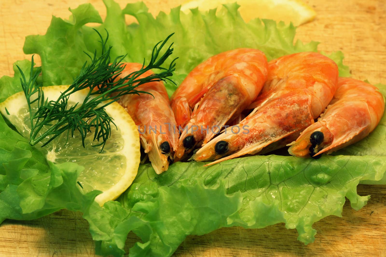 Closeup of cooked shrimps, lemon, greens and lettuce lying on wooden plate