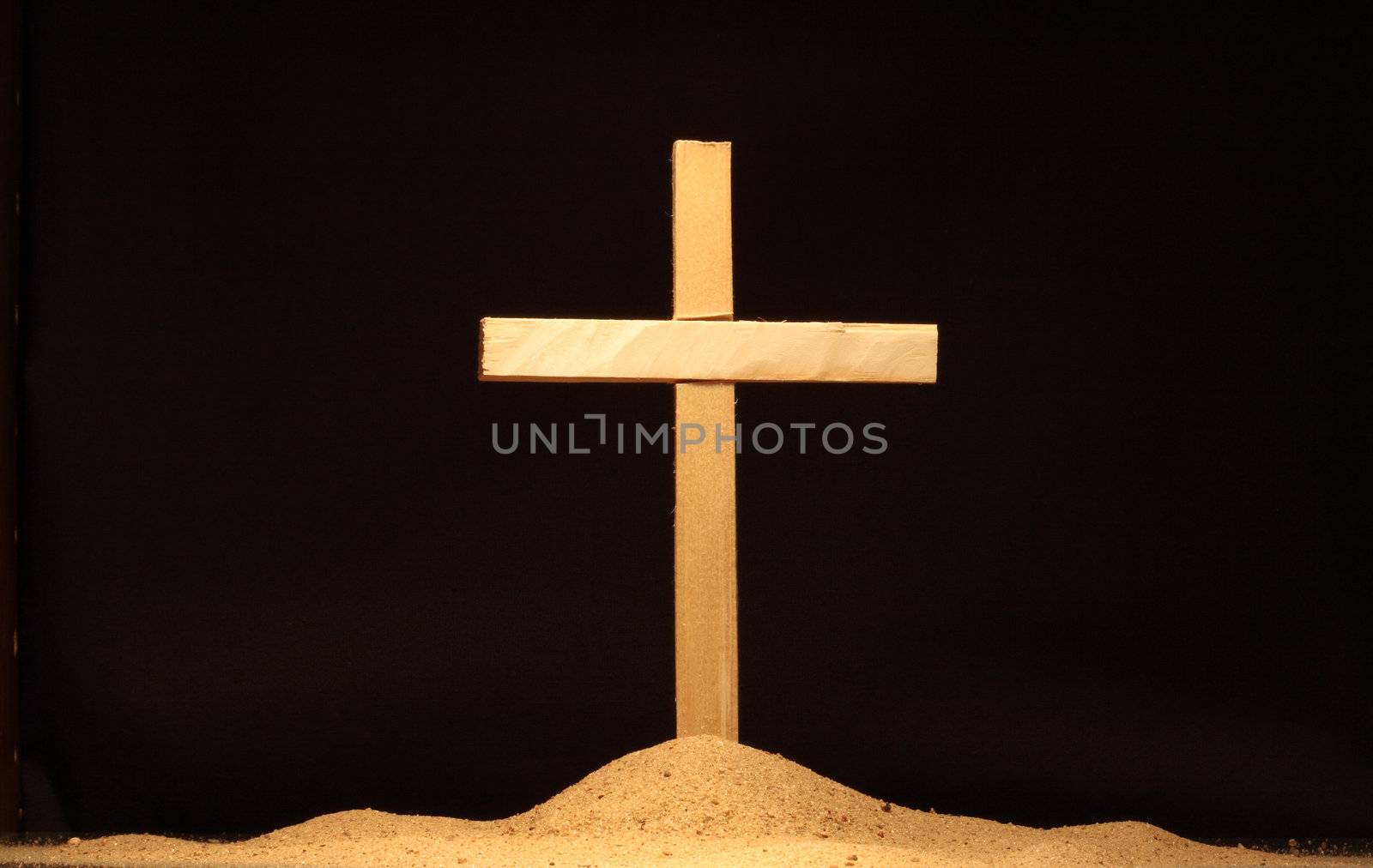 Single wooden cross in sand isolated on black background