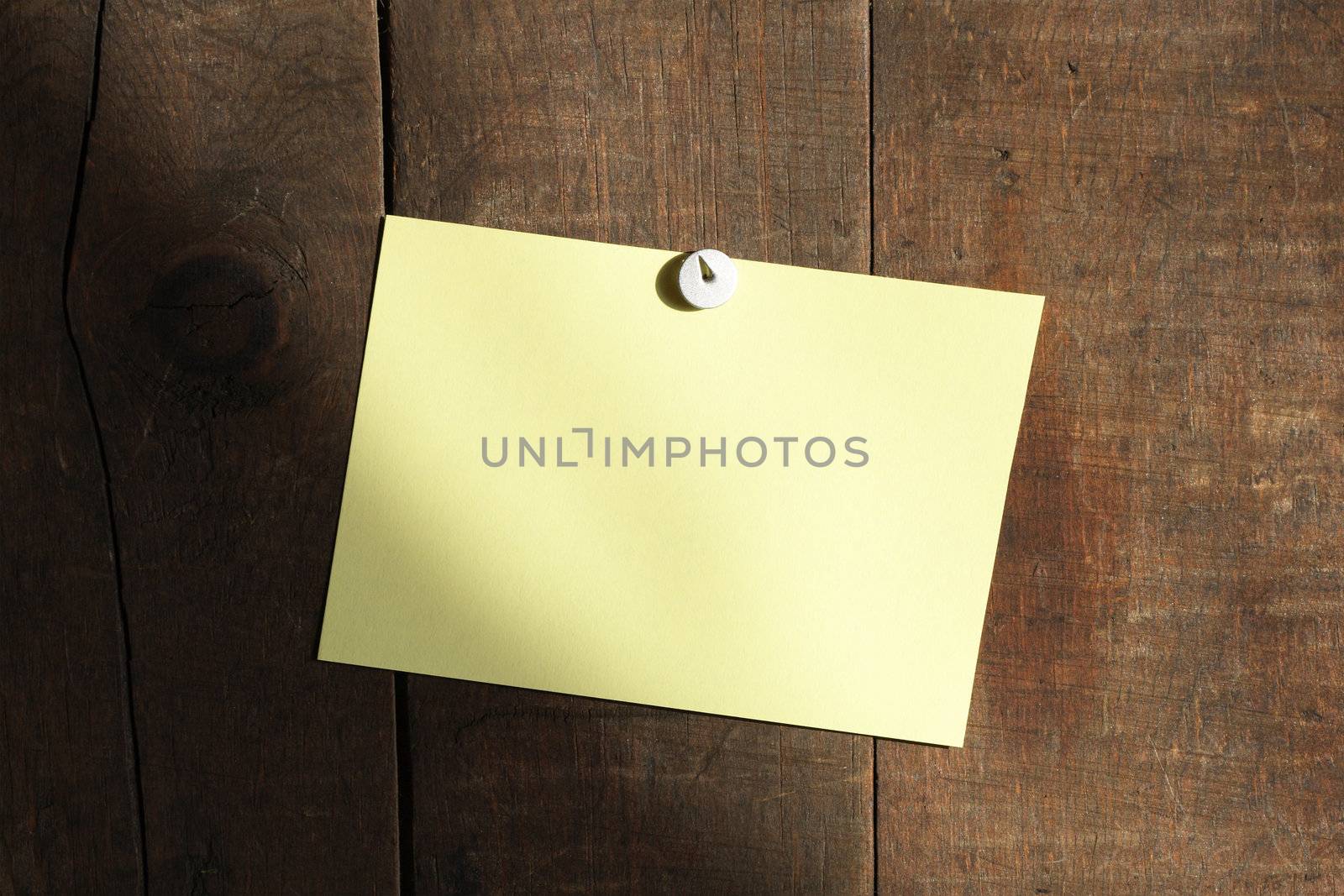 Yellow note paper hanging with thumbtack on wooden background 