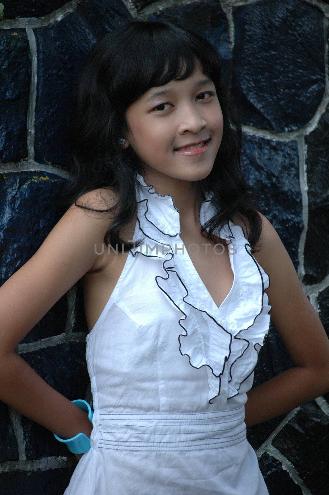 little asian girl stand up beside rock wall in park
