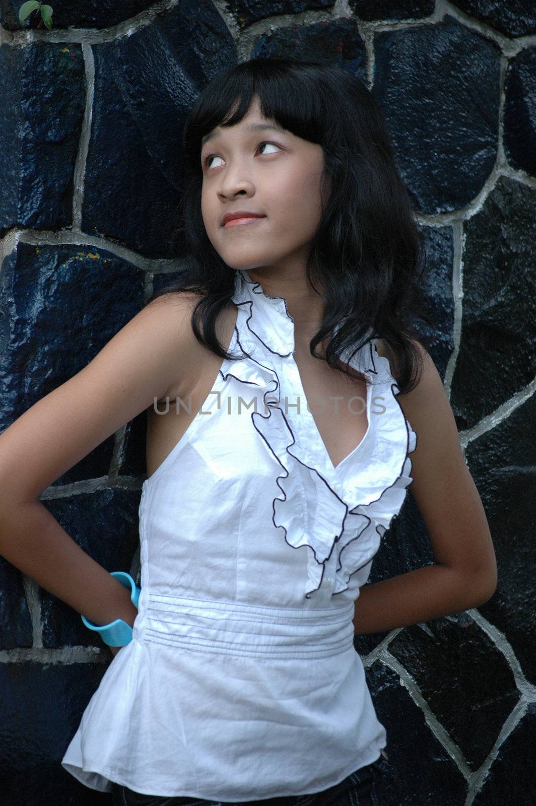 little asian girl stand up beside rock wall in park
