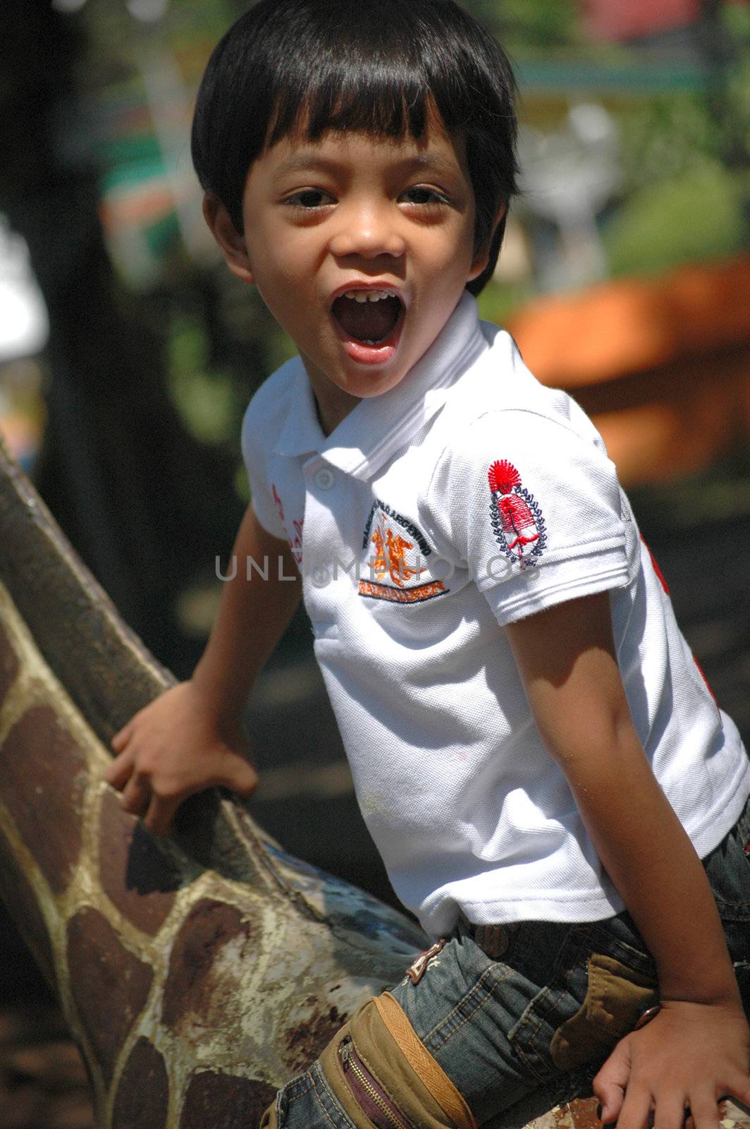 little asian boy sit down on zeebra statue in park
