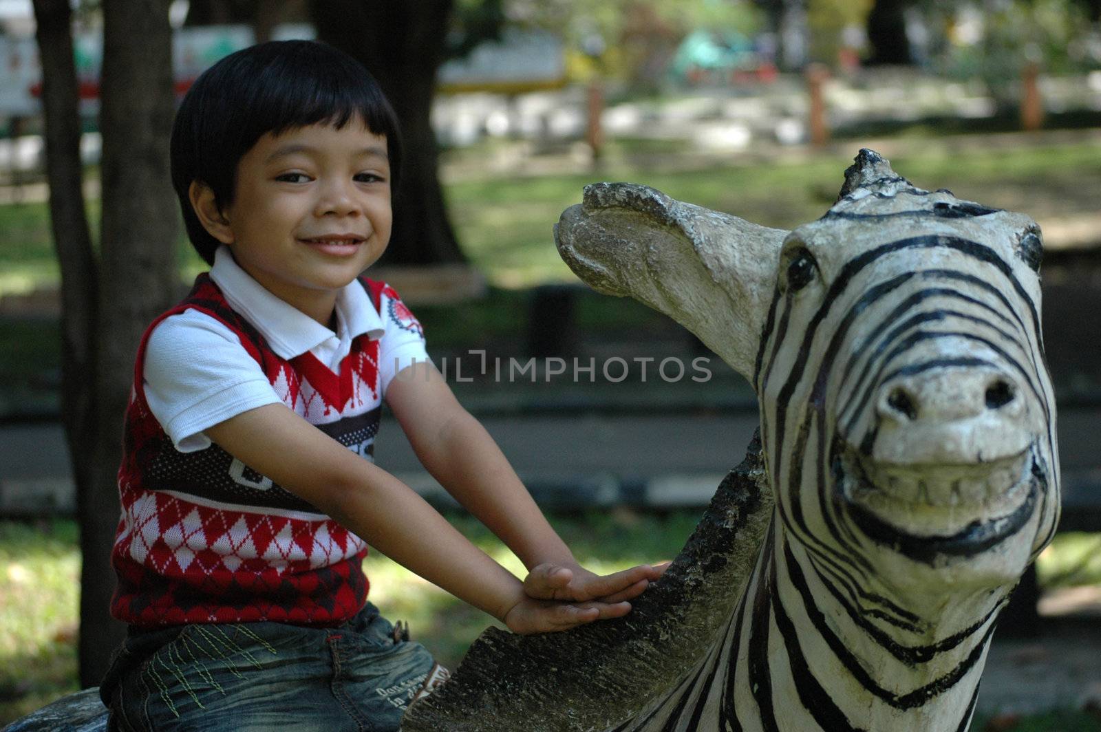 little asian boy sit down on zeebra statue in park
