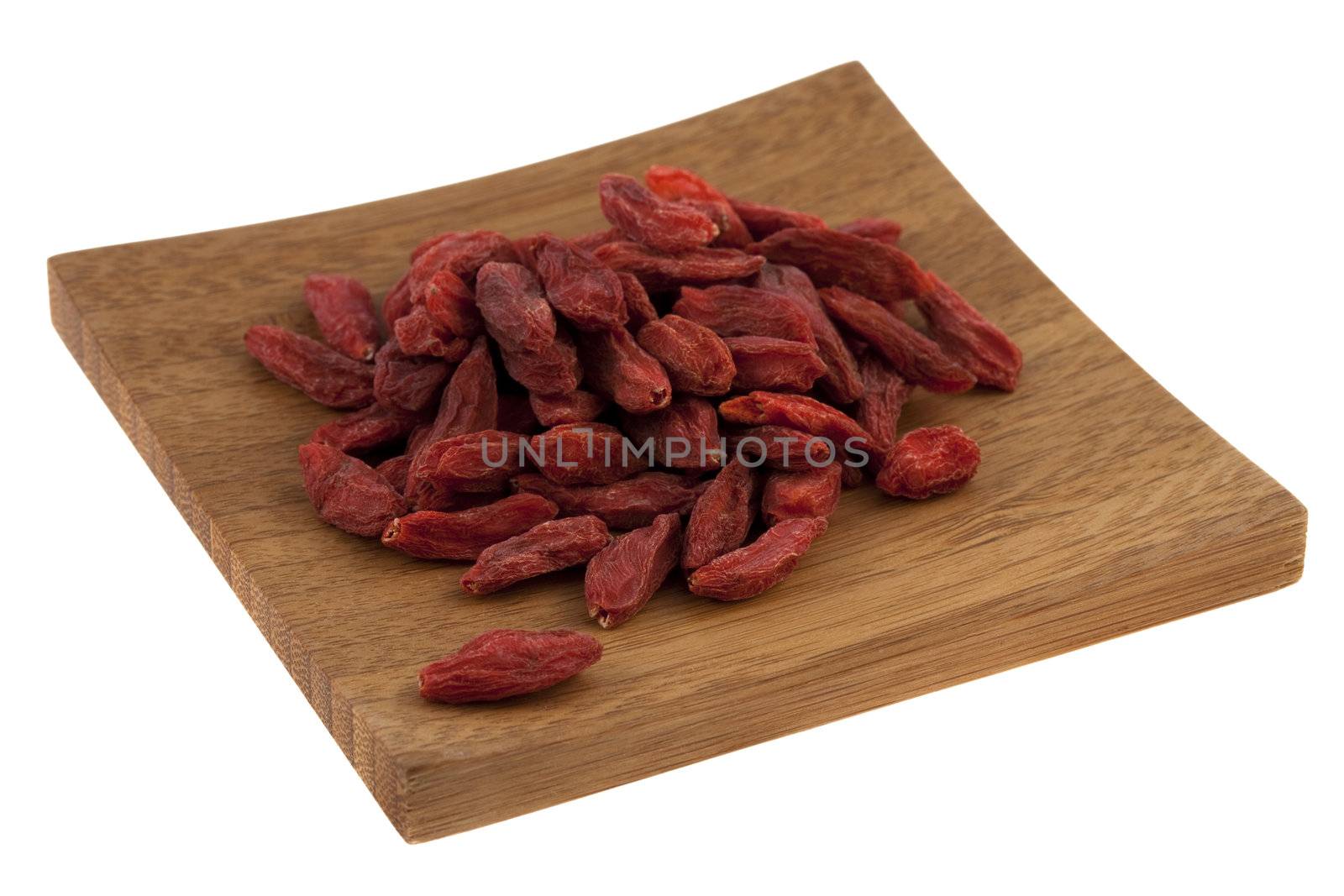 a pile of dried Tibetan goji berries (wolfberry) on a small wooden square tray isolated on white, selected focus on fruits