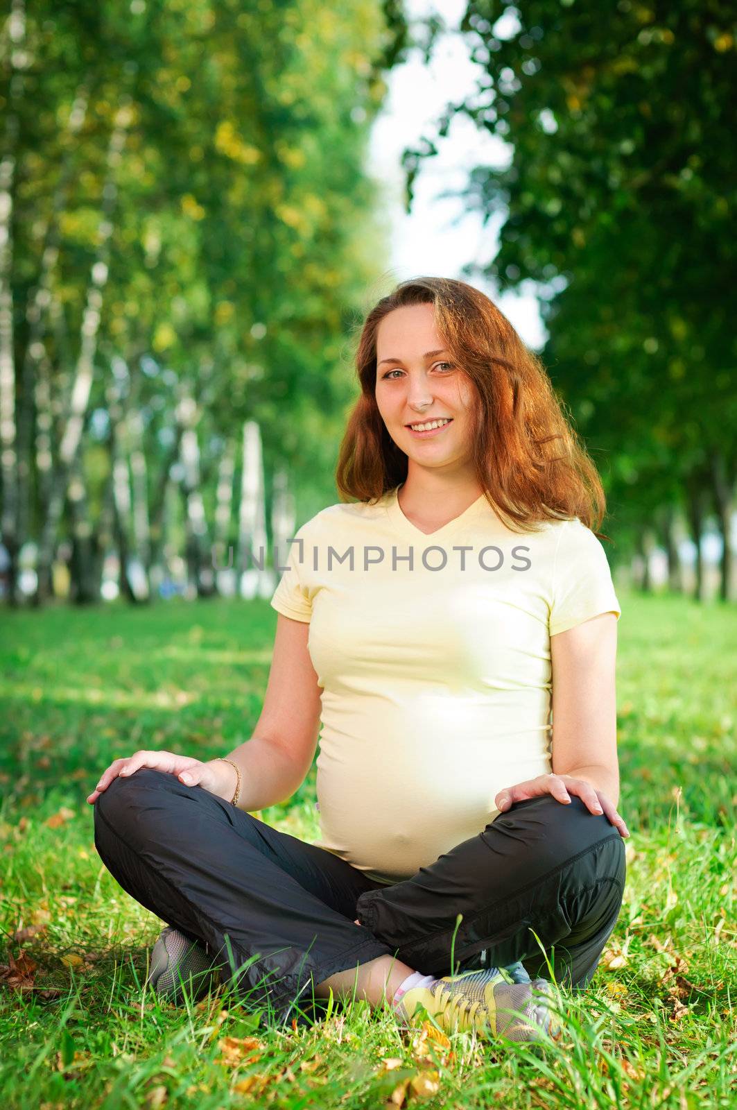 Beautiful pregnant woman relaxing on the grass in the park