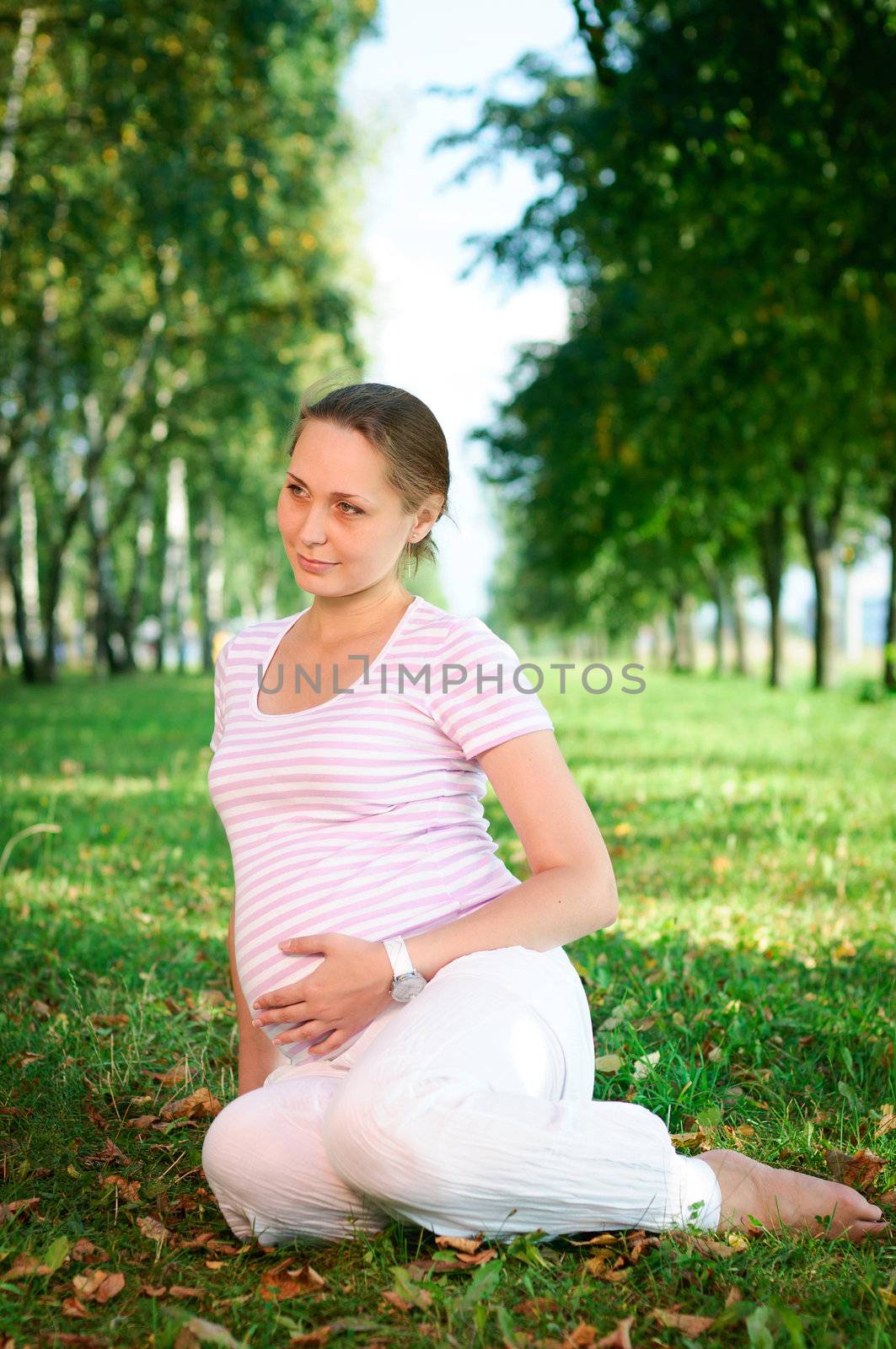 Beautiful pregnant woman relaxing on the grass in the park