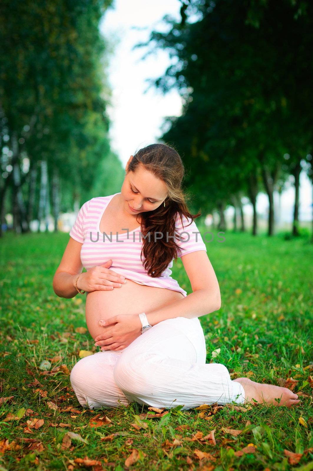 Beautiful pregnant woman relaxing on the grass in the park