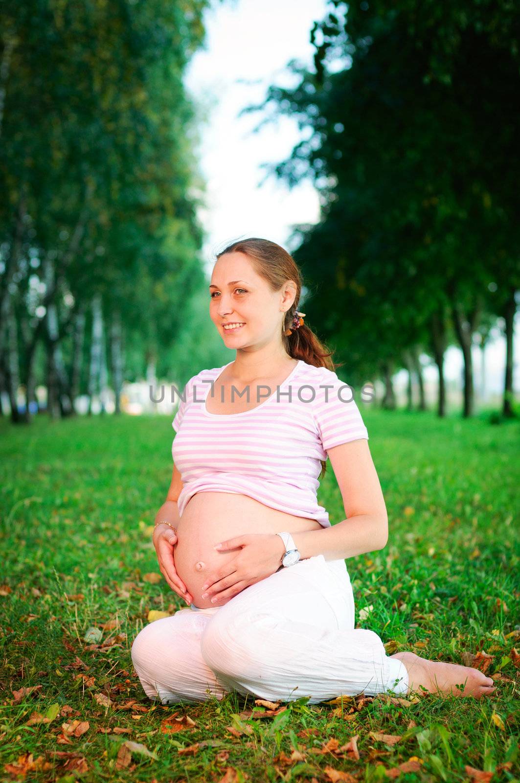 Beautiful pregnant woman relaxing on the grass in the park