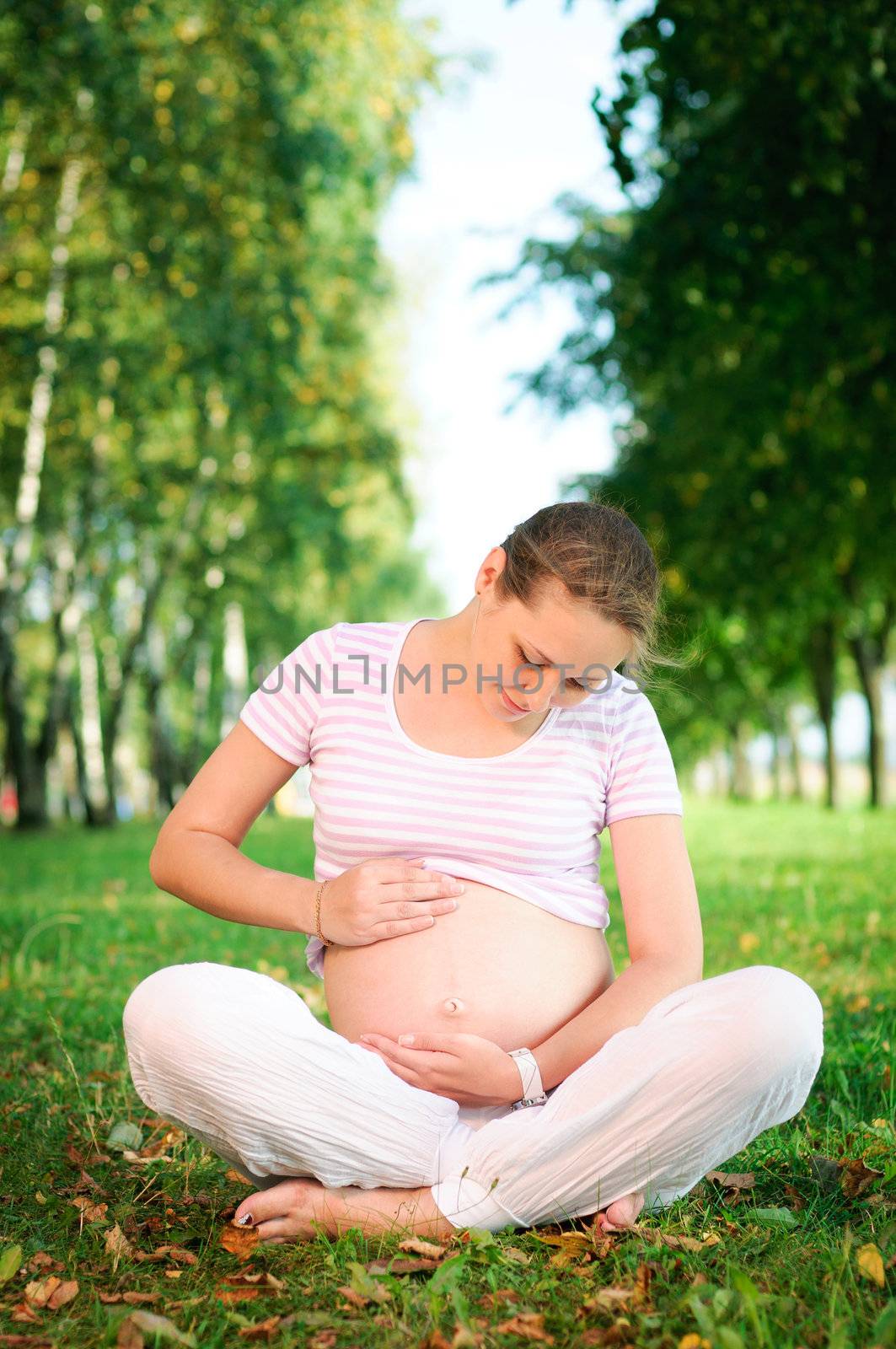 Beautiful pregnant woman relaxing on the grass in the park