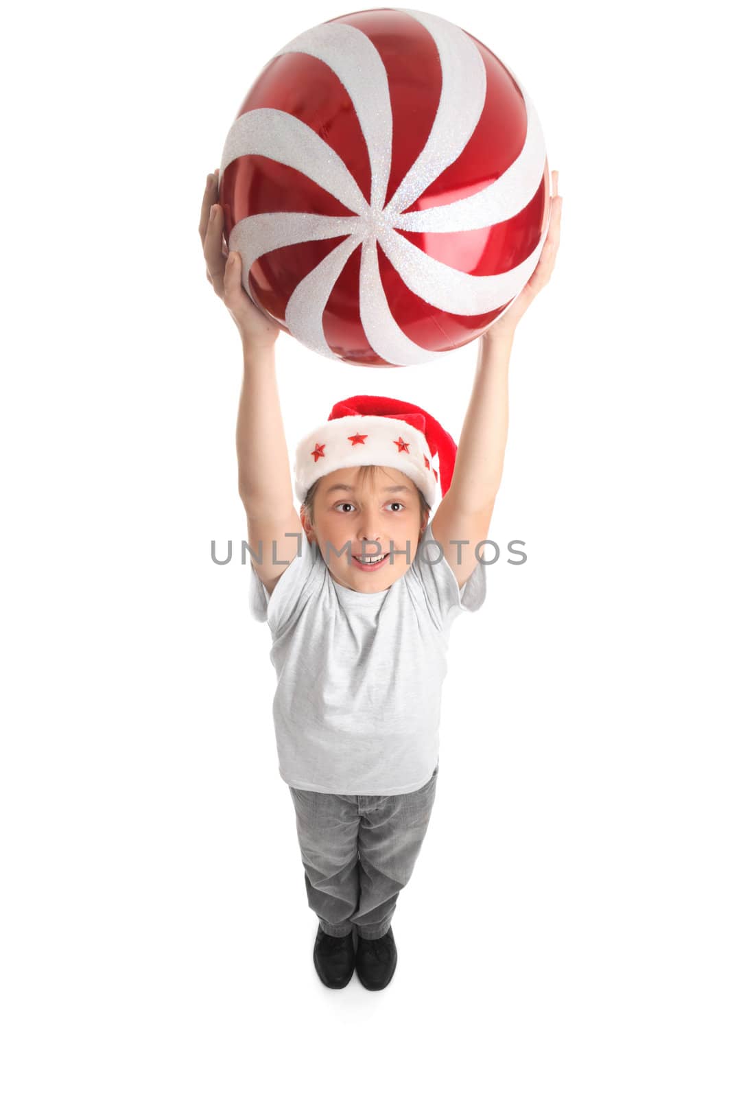 A smiling boy holding a large Christmas bauble in two hands above his head.