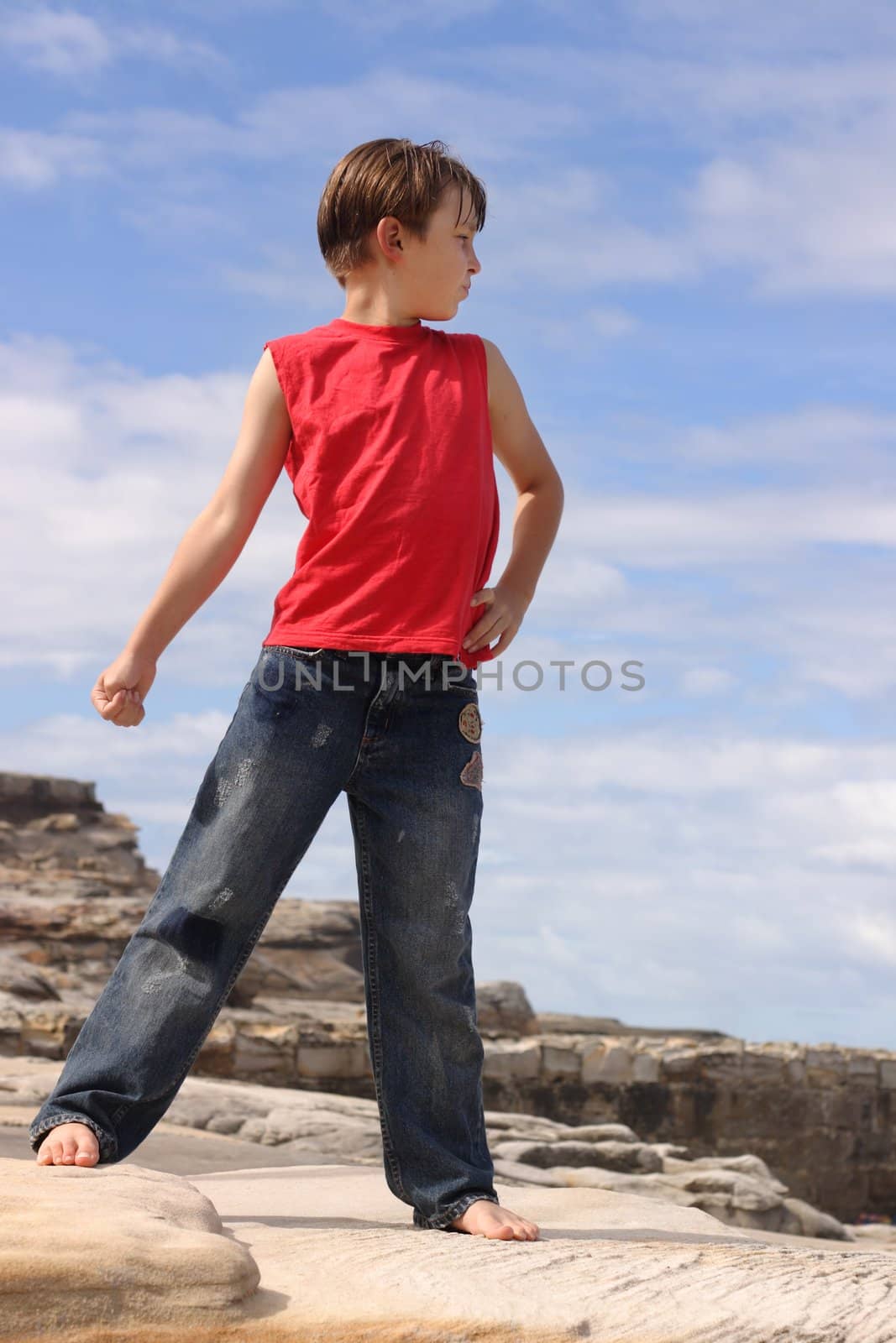 Child outdoors in the summer sun standing on rocks with a pretty blue sky and clouds behind him.