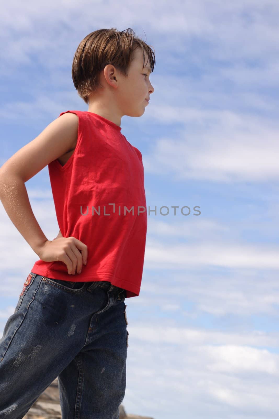 A boy stands hands on hips against a blue sky