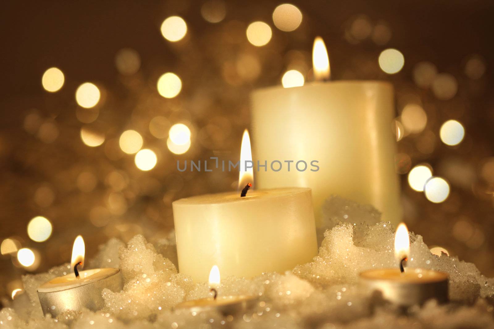 Brightly lit candles in wet snow against sparkly background