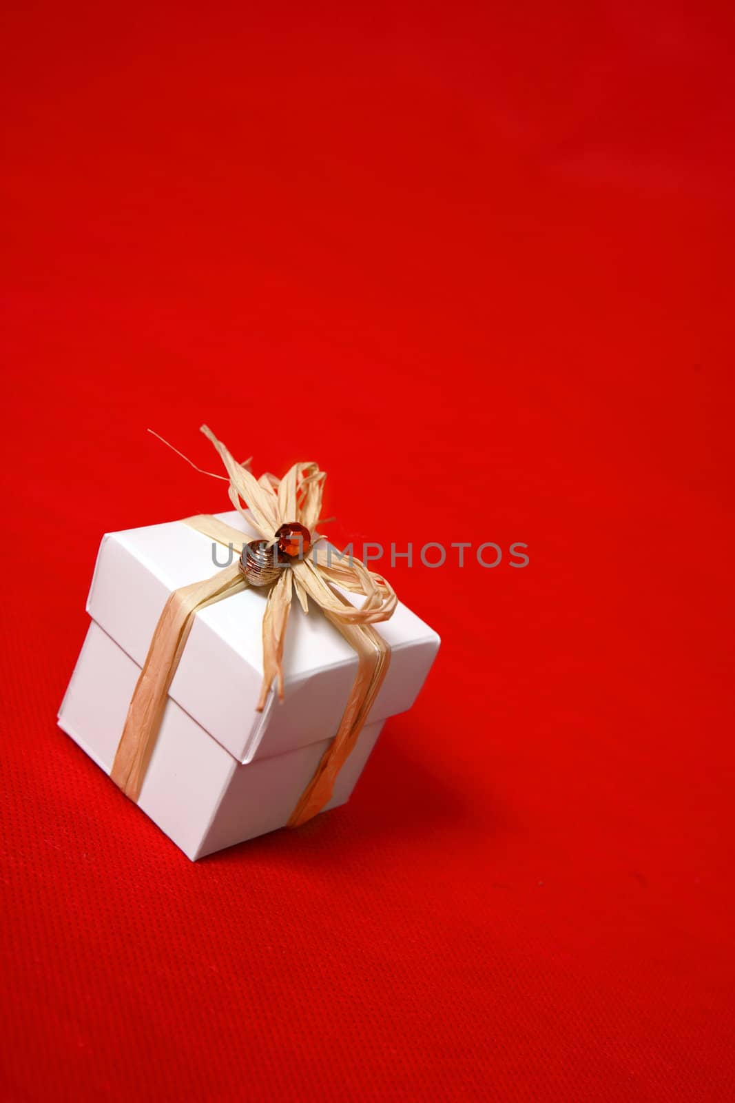 A white gift box tied with raffia and decorated with beads sits on a red background.  Suitable for birthday, Christmas, valentine,  or other special occasions.