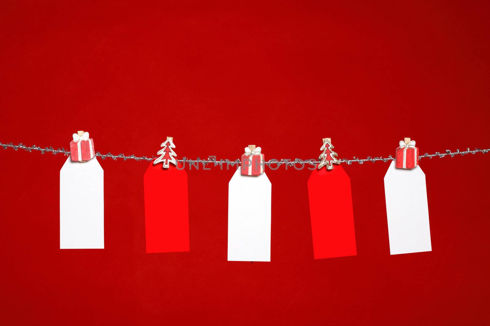 Festive red and white tags hanging from silver tinsel  line on a red background